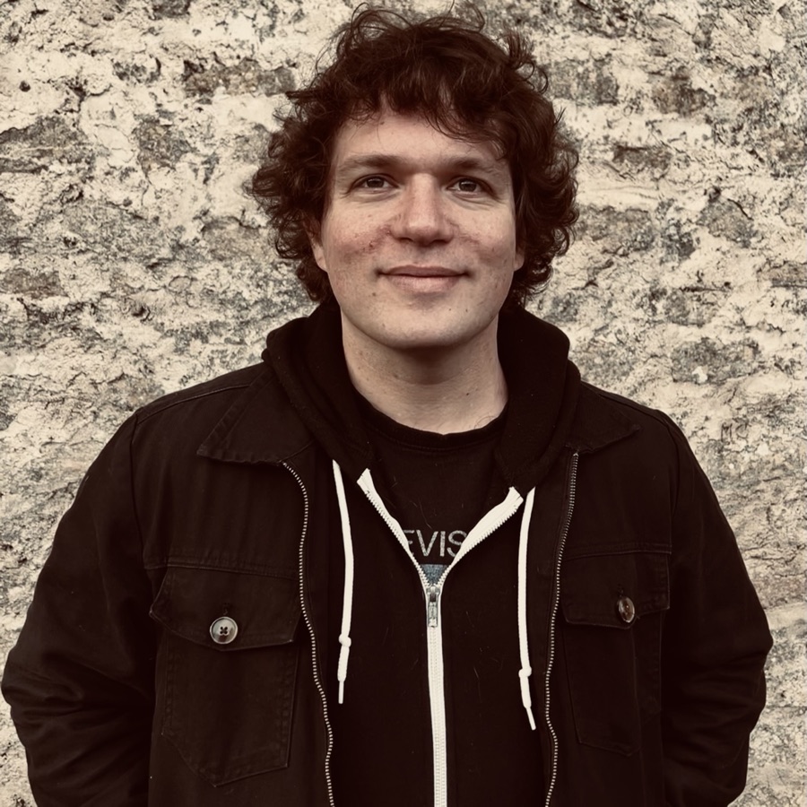Cris Slotoroff in a dark jacket, standing in front of a stone wall